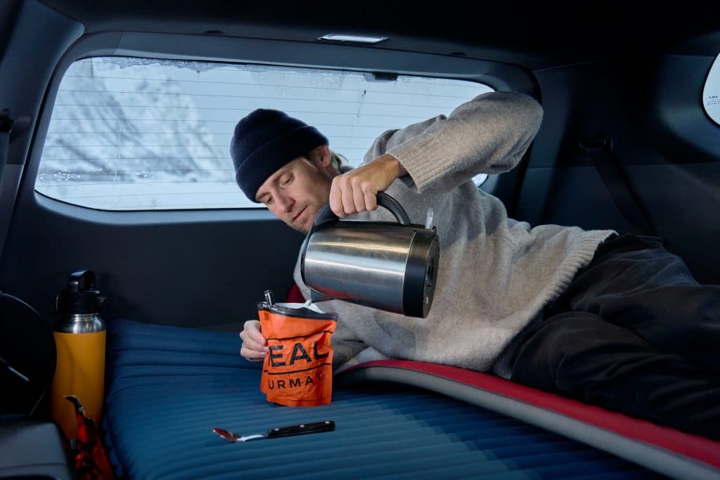 Surfaren Tim Latte ligger i baksätet på sin Kia EV9 och värmer sin mat.